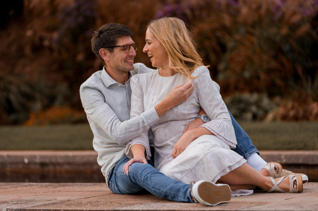 engaged couple playing around with each other while sitting on the payment way through the water in the gardens of their summer engagement