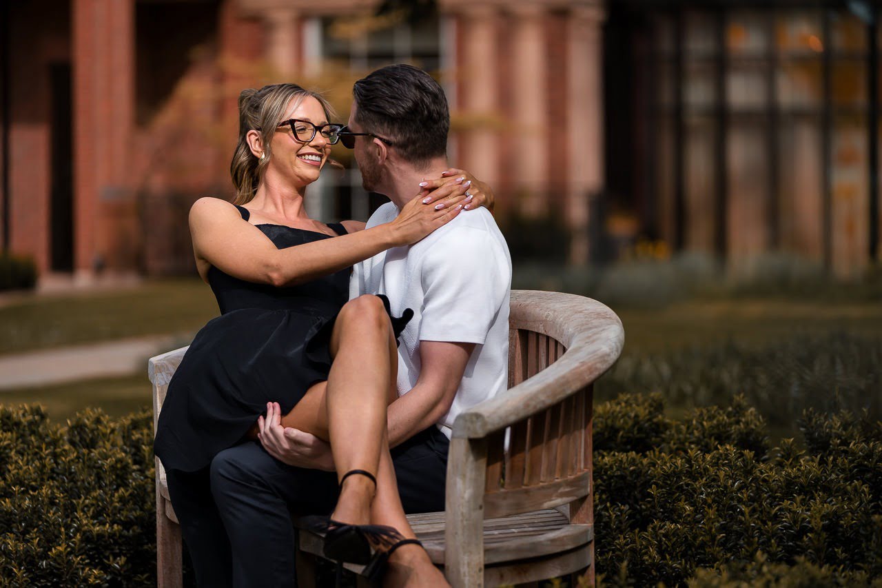 engaged couple sitting & cuddling on a wooden bench for a spring engagement shoot at the Grove Hotel