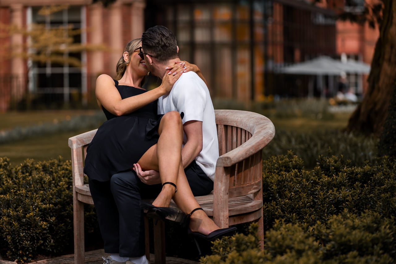 engaged couple sitting and kissing on a wooden bench for a spring engagement shoot at the Grove Hotel
