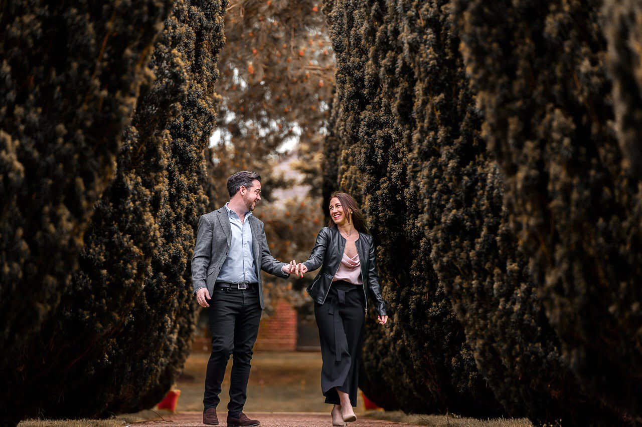couple swinging arms as they walk down an avenue of trees at the grove