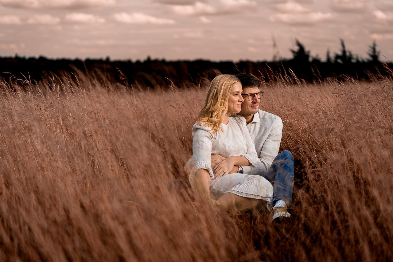 couple sitting next to each other in the tall golden grasses at the grove hotel hertfordshire