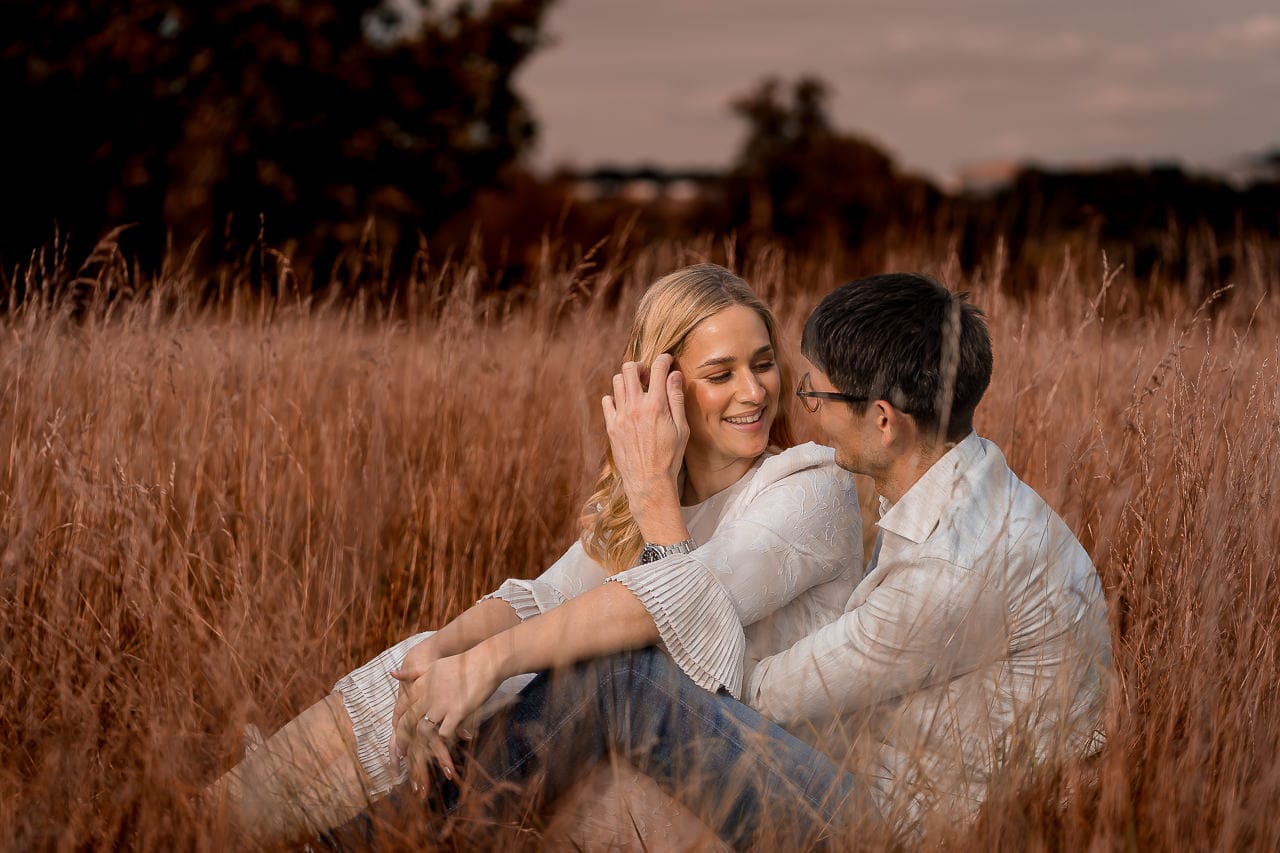 couple laying on to each other in the tall golden grasses, woman pushing back her hair in the wind