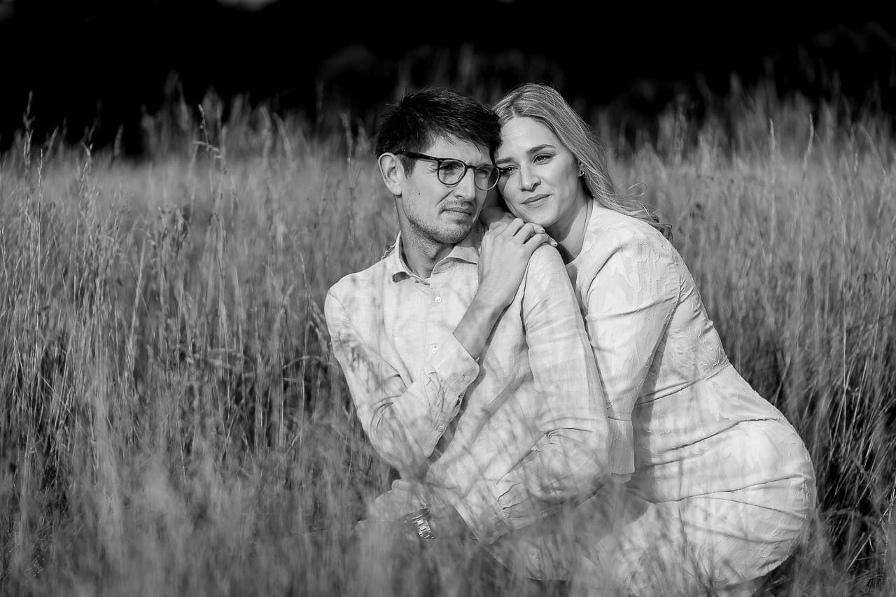 black and white photo of couple laying on to each other in the tall golden grasses of their summer engagement