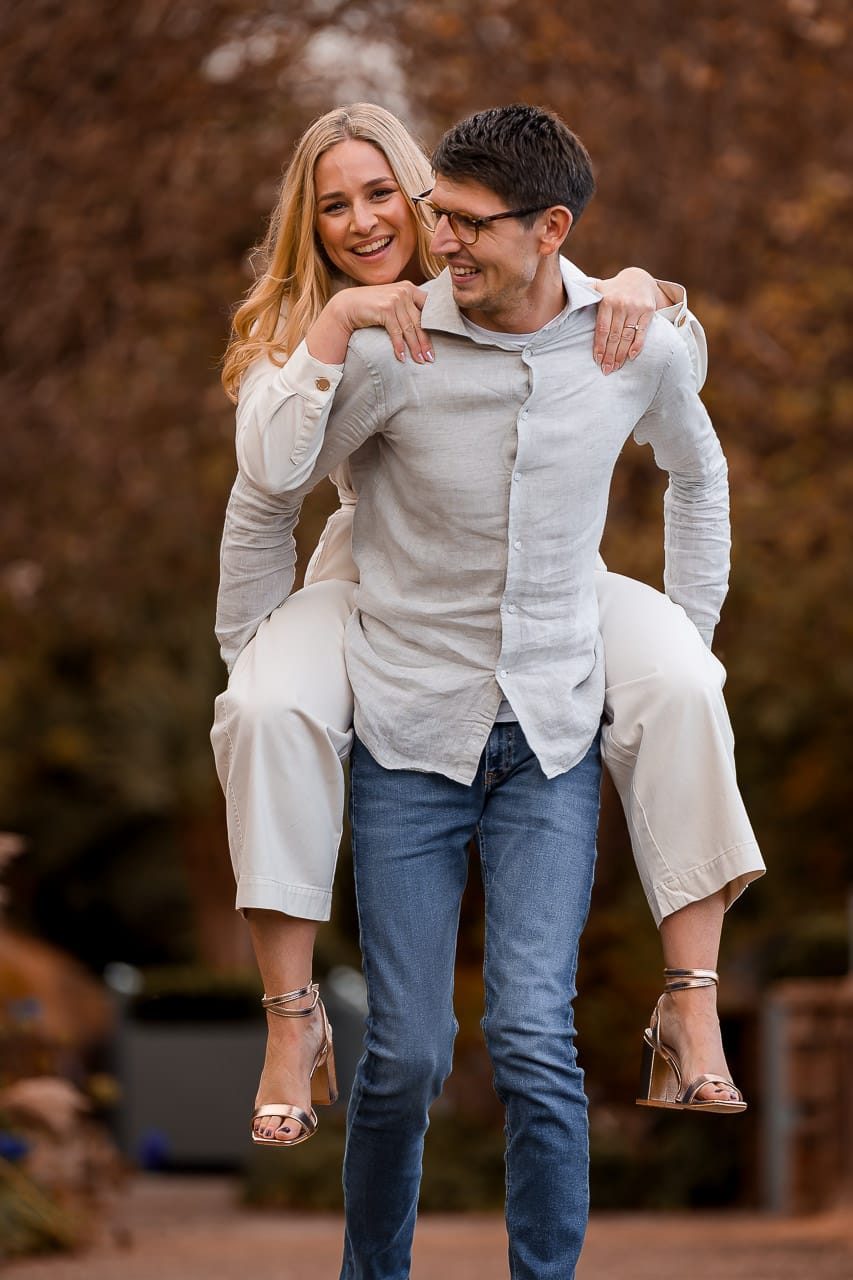 man giving a woman a piggy-back ride through the gardens at the Grove Hertfordshire for their summer engagement session