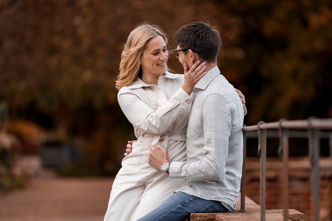 man and woman facing each other, a man sitting on a wall, at their summer engagement session