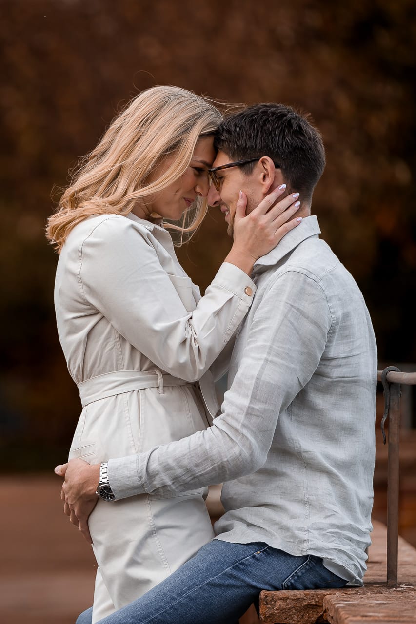 man and woman facing each other, a man sitting on a wall, and their foreheads together at their summer engagement session